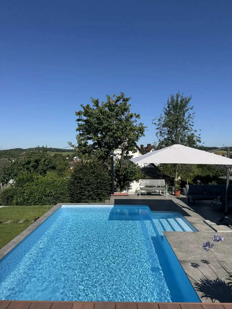 Pool mit dunkler Steinterrasse, Lounge und Sonnenliege, im Hintergrund die Hügel der Region Trier
